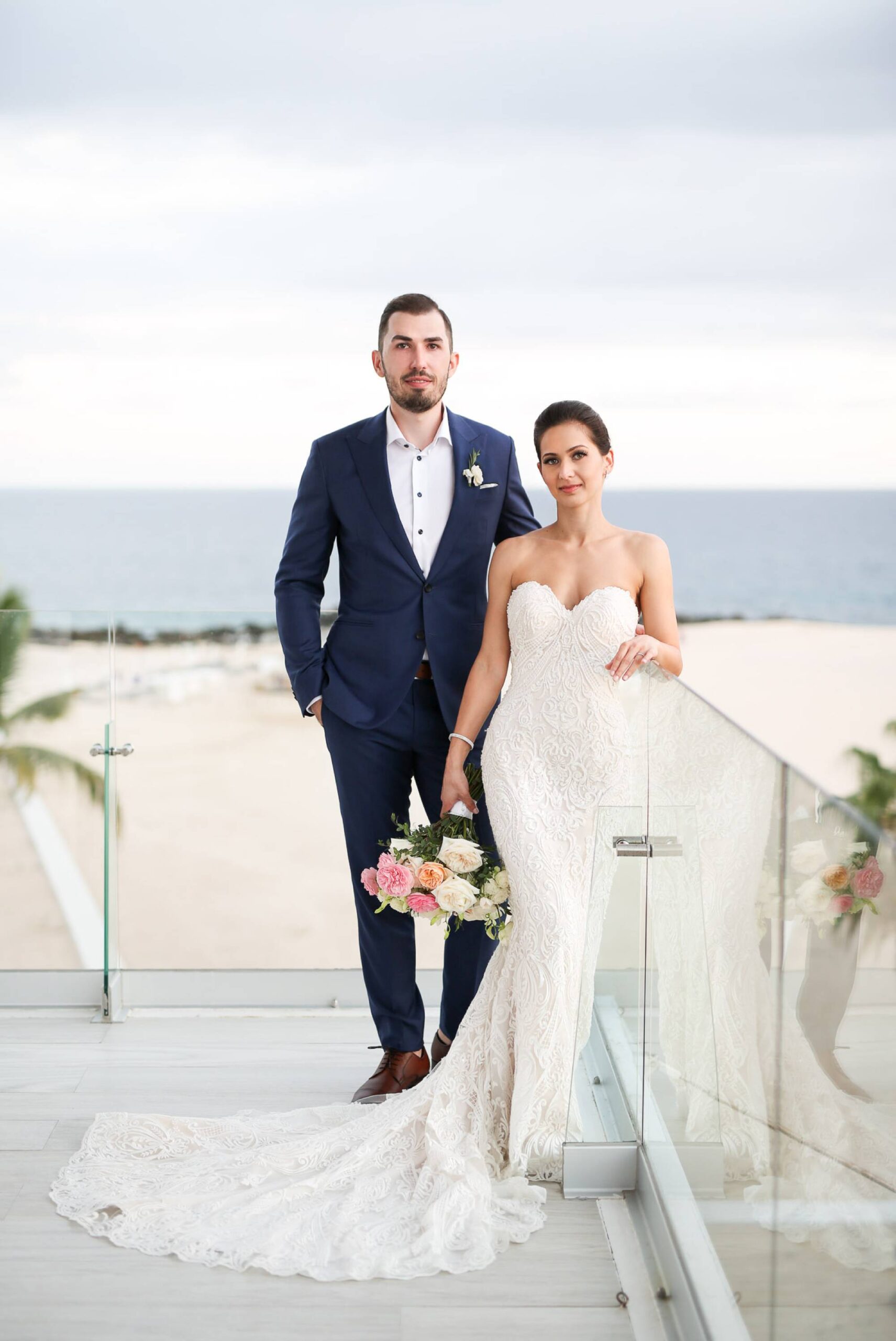 Bride and groom portrait on reception balcony with glass railings and beach and ocean behind