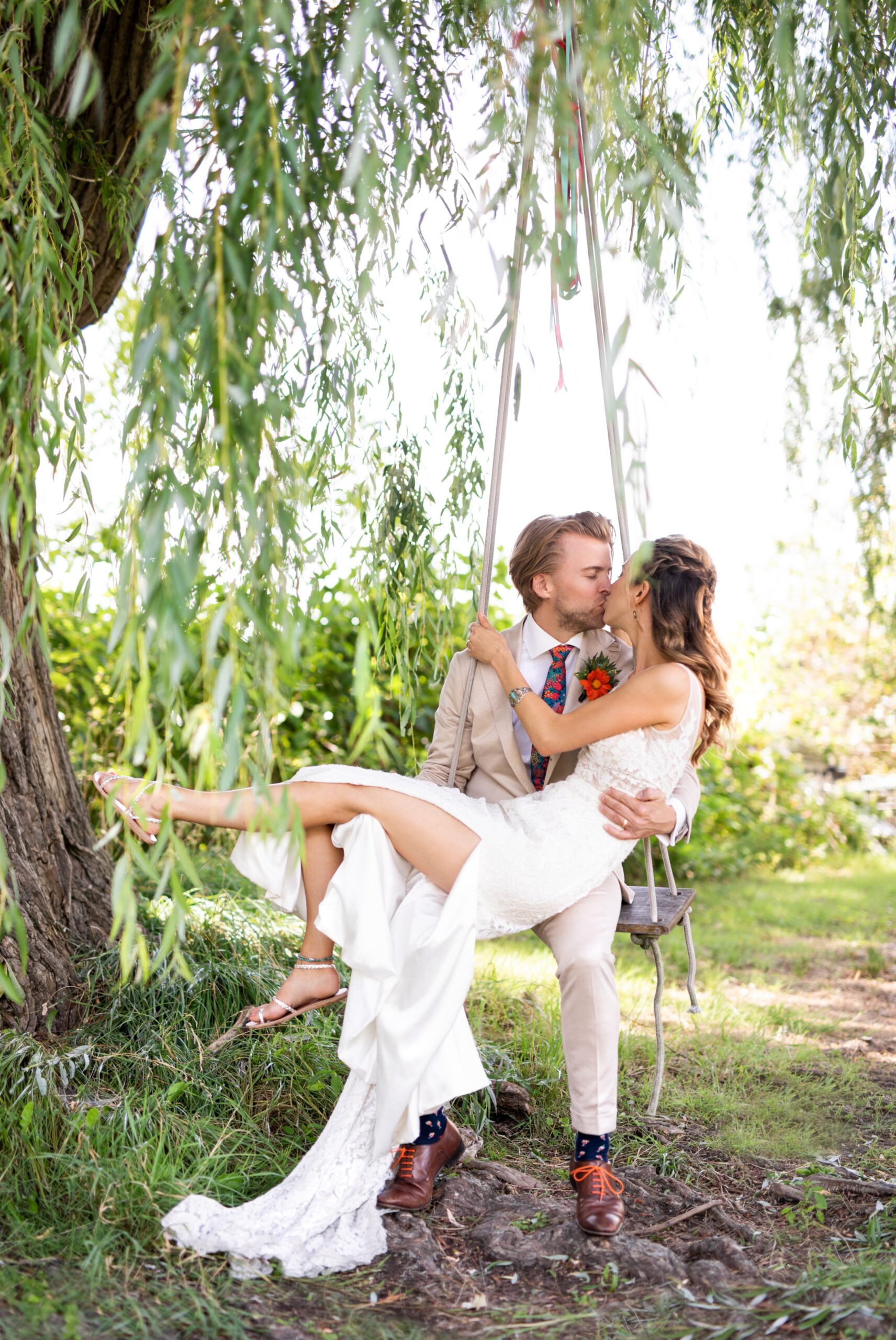 Wedding couple sit on swing on willow tree and kiss