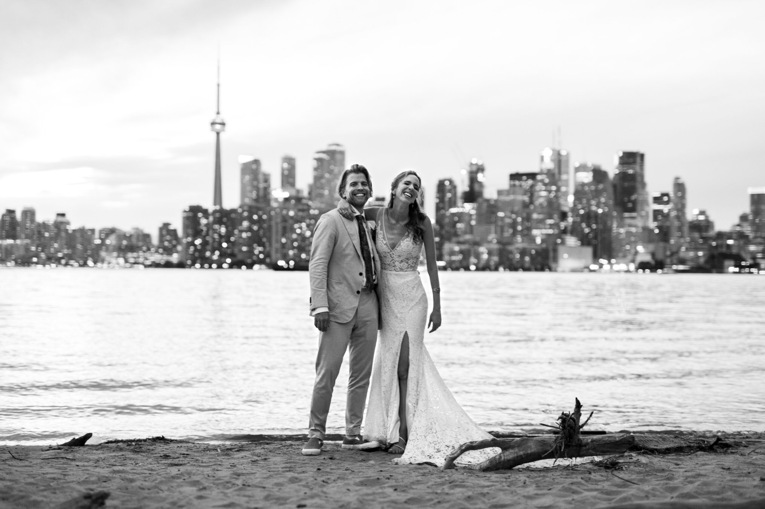 black and white portrait of couple smiling in front of toronto skyline sunset on beach